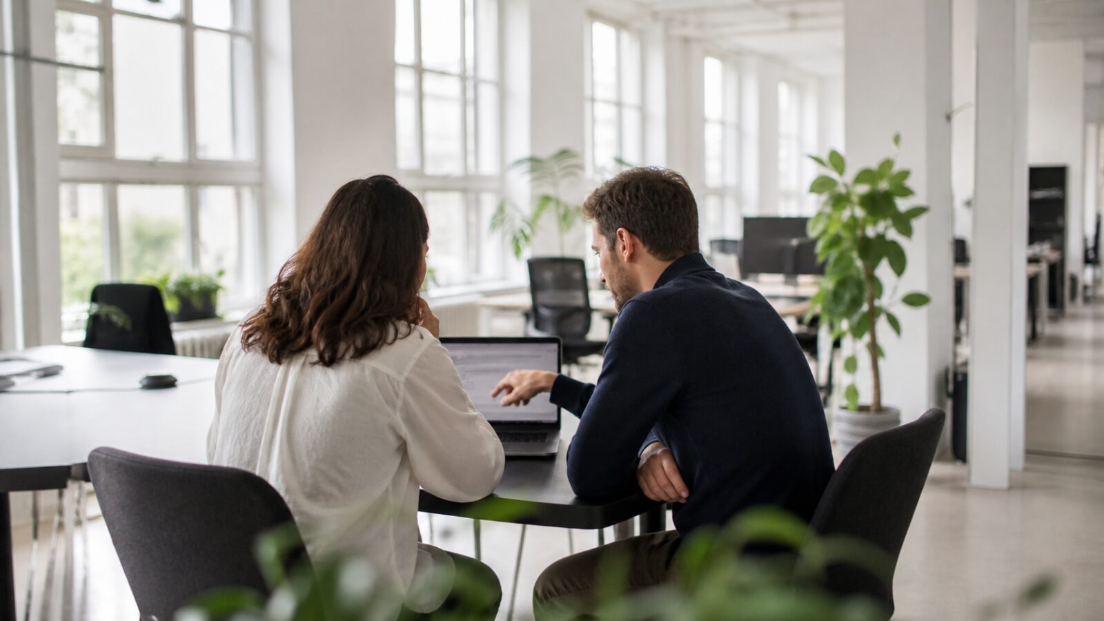 Deux collègues comparent ensemble des offres d'abonnement logiciel sur un ordinateur portable dans un bureau lumineux
